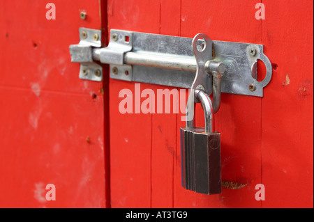 neue Hasp und Grundnahrungsmittel mit Vorhängeschloss angebracht, um eine rot bemalte Holztür in Belfast City Centre zu sichern Stockfoto