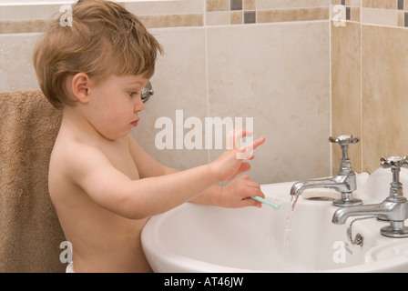junge Kleinkind zweiundzwanzig Monate alt waschen Hände am Waschbecken im Badezimmer mit Armaturen und Wasser spielen Stockfoto