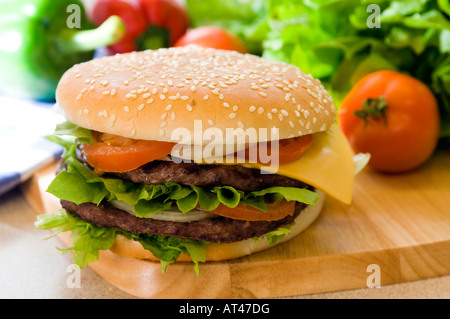 Einen heißen Doppel-Käse-Burger mit Salat Tomate & Zwiebeln, mit frischen Produkten auf einer hölzernen Platte vorgestellt Stockfoto