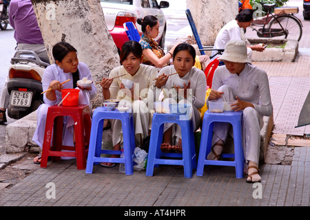 Asien Fernost Vietnam, Saigon, vier ziemlich lächelnde junge Mädchen der Schule Teenager-Stop für Snack in der Straße tragen traditionelle Kleidung, AO dai Stockfoto