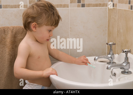 junge Kleinkind zweiundzwanzig Monate alt waschen Hände am Waschbecken im Badezimmer mit Armaturen und Wasser spielen Stockfoto