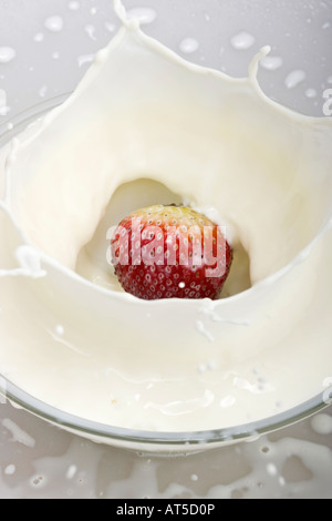 Nahaufnahme der roten Reifen Erdbeere, die in die Milch fällt mit Spritzern Farbkonzept von oben oben oben niemand keine vertikale Hochauflösung Stockfoto