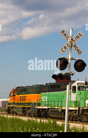 Ein Güterzug BNSF bewegt sich langsam vorbei an einer Kreuzung Schutzbarriere in einer kleinen Seitenstraße in einem Vorort von Chicago. Stockfoto