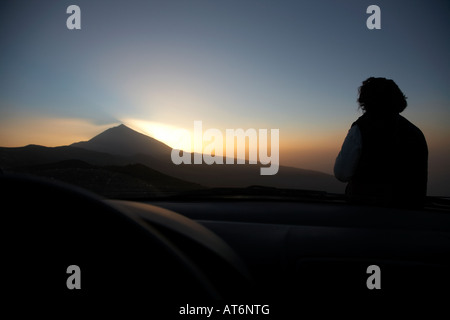Frau sitzt auf der Motorhaube eines Autos beobachten den Sonnenuntergang über den Teide el Tiede Teneriffa Kanaren Spanien Stockfoto