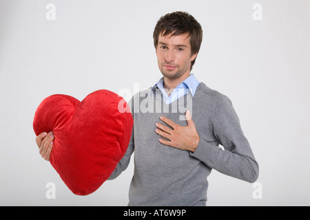 Junger Mann Betrieb herzförmige Kissen, portrait Stockfoto