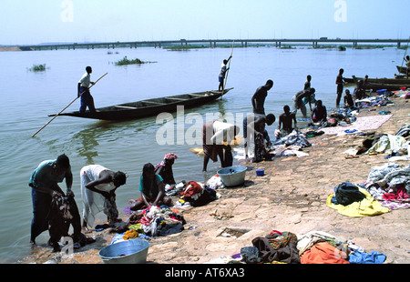 Männer, die eine Piroge mit Pfählen pochten und Männer und Frauen am Ufer des Nigers in der Hauptstadt Bamako waschen. Mali Stockfoto