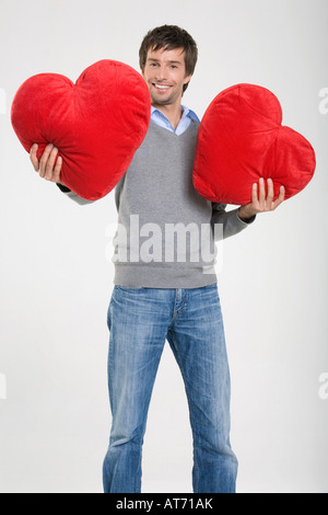 Junger Mann Betrieb herzförmige Kissen, portrait Stockfoto