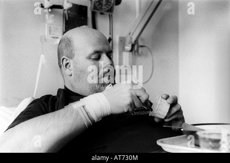 Großer Glatzenbildung bärtiger Mann im Krankenhaus kratzt die letzten Bissen aus einem Pappbecher. Stockfoto