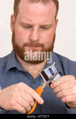 Junger Mann zerschneidet Kreditkarten mit einer Schere Stockfoto