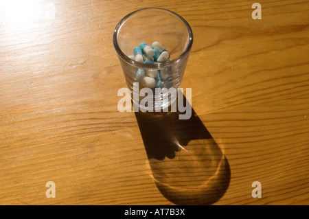 Prozac in einem Schnapsglas mit einem Schatten auf der Oberfläche des Holzes. Stockfoto