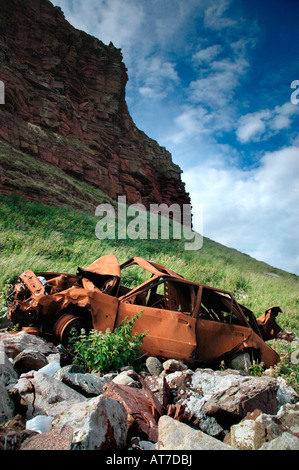 Ein verrostetes Auto liegt auf Gestein am Fuße der Klippen, von wo es aus gedrückt worden ist. Stockfoto