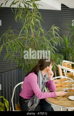 junge Frau sitzt auf einem Stuhl in der Nähe von Zierpflanzen gekleidet in Freizeitkleidung mit rosa Bluse suchen abgelenkt Stockfoto