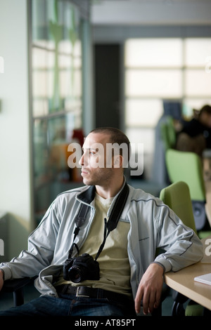 junger Mann mit einer Kamera sitzt auf einem Stuhl neben einem Tisch mit Blick auf das Licht Stockfoto