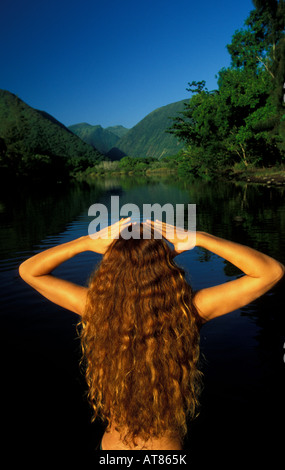 Rückseite einer jungen Frau mit langen fließenden braunen welliges Haar am Bach, der an der Rückseite des Waipio Valley, North Kohala führt, Stockfoto