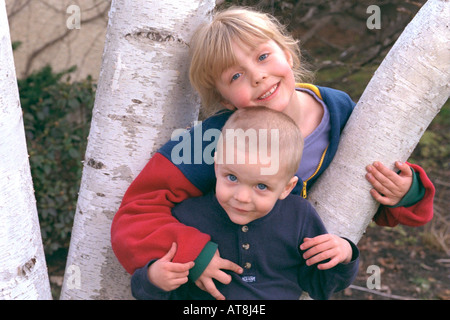 Lächelnde Schwester und Bruder in Birke Baum Alter 3 und 6 spielen. St Paul Minnesota USA Stockfoto