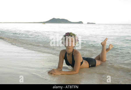 Schöne junge Frau trägt einen schwarzen Badeanzug lounges am Ufer am weltberühmten Strand Lanikai auf der windzugewandten Seite von Oahu. Stockfoto