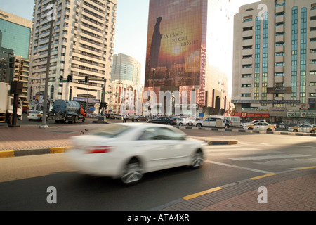 Ein weißes Auto fahren auf der Straße Geschwindigkeiten vor Wolkenkratzer, Stadtzentrum Abu Dhabi, Vereinigte Arabische Emirate Stockfoto