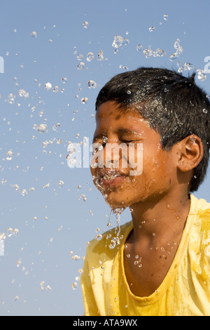 Indianerjunge Spritzwasser auf seinem Gesicht vor einem blauen Himmel. Indien Stockfoto