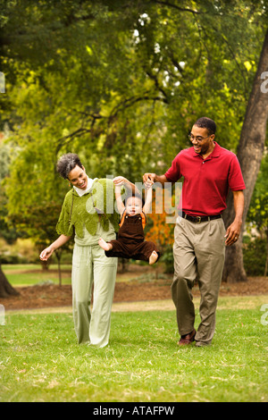 Mutter und Vater schwingen Kleinkind seine Händchen im park Stockfoto