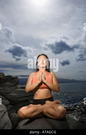 Asiatische Frau sitzt auf Felsen vom Ozean in Lotus-Pose mit geschlossenen Augen in Maui Hawaii Stockfoto