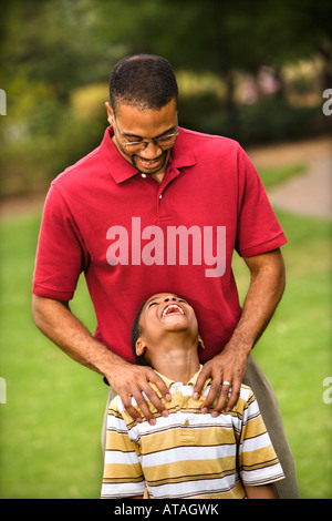Vater Sohn mit den Händen auf seinen Schultern als junge lächelt hinter Stockfoto