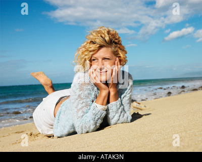Attraktive junge, blonde Frau, liegend im Sand am Strand von Maui Hawaii mit Kopf auf Händen Stockfoto