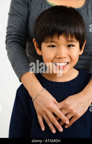 Porträt von Asian Boy mit Mutter stehend hinter mit Arme um ihn lächelnd Stockfoto