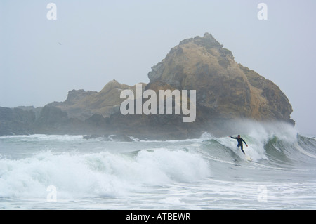 Mann beim Surfen auf die brechenden Wellen neben Küste Felsen im Nebel Pfeiffer Beach Big Sur Küste Monterey County Kalifornien Stockfoto