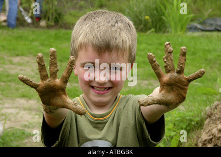 Kind von einer Grundschule hat einen Ofen aus Brickearth zeigt seine schmutzigen Händen bauen Stockfoto