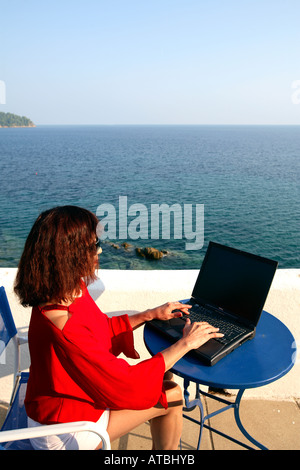 GRIECHENLAND-FRAU MIT EINEM LAPTOP AUF ABGELEGENEN VILLA TERRASSE MIT BLICK AUFS MEER Stockfoto