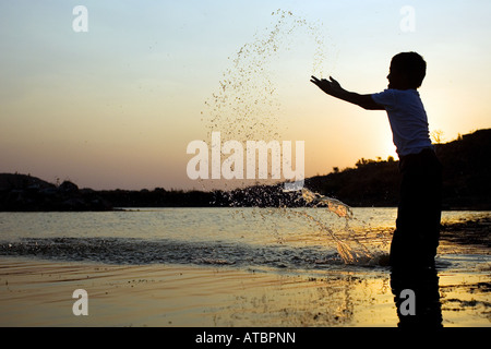 Indianerjunge Spritzwasser in einem See in Indien bei Sonnenuntergang. Indien Stockfoto