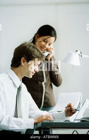 Männlichen und weiblichen Kollegen Blick auf Laptop-Computer zusammen, Mann zeigte mit Stift, Frau mit Telefon Stockfoto