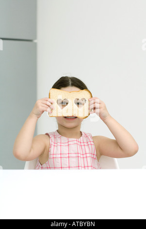 Kleines Mädchen hält Brot mit herzförmigen Cut Outs, durch Löcher in die Kamera schauen Stockfoto