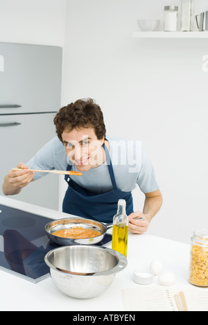 Mann in Küche, beugte sich über Geschmack Sauce, lächelnd in die Kamera Stockfoto