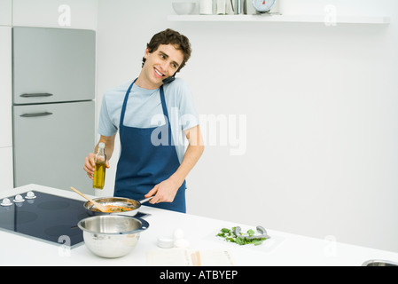 Junger Mann am Herd kochen, mit Handy, Lächeln Stockfoto