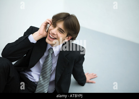 Junger Mann im Anzug auf dem Boden sitzend mit Handy, Lächeln Stockfoto