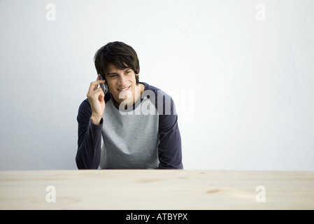 Junger Mann sitzt am Tisch, mit Handy, Lächeln Stockfoto