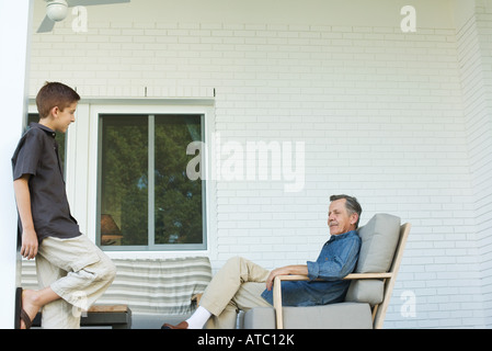 Großvater und Enkel zusammen auf Terrasse, stehend, junge Mann sitzend Stockfoto