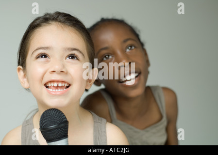 Zwei junge Mädchen singen in Mikrofon zusammen, lächelnd und das Nachschlagen Stockfoto