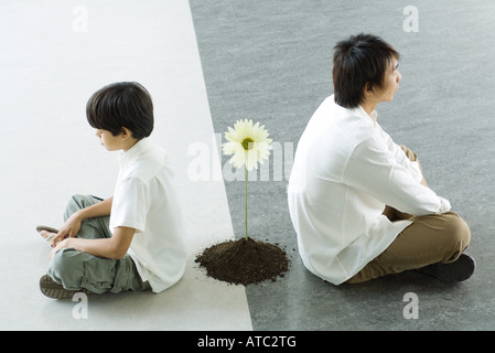 Junge und Mann sitzen Rücken an Rücken, eine einzelne Blume zwischen Ihnen Stockfoto