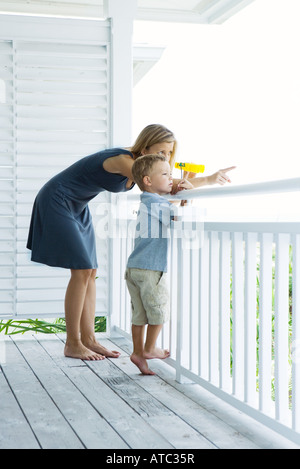 Mutter und Sohn auf Veranda stehen zusammen, Frau halten Ferngläser und zeigen beide wegschauen Stockfoto