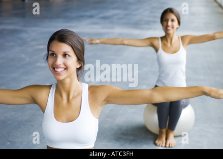 Teenager Zwillingsschwestern auf Fitness Kugeln sitzen, Arme ausgestreckt, beide Lächeln Stockfoto