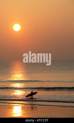 ein einsamer Surfer zu Fuß ins Meer bei Sonnenuntergang Stockfoto