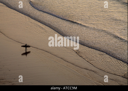 eine Surfer mit seinem Brett geht durch einen leeren Strand in Richtung Meer Stockfoto