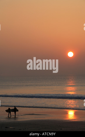 zwei Surfer zu Fuß am Strand mit den Sonnenuntergang über dem Meer Stockfoto