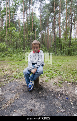 Kleiner Junge saß allein auf Baumstumpf im Wald, im Wald spielen Stockfoto