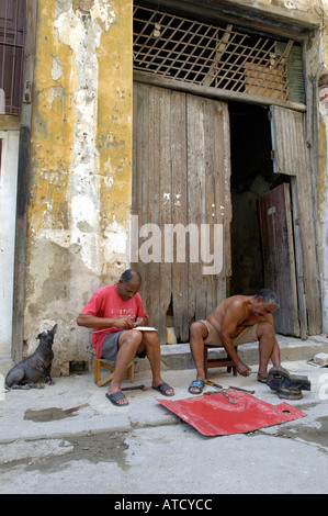 Zwei Männer in Habana Vieja, Kuba sitzen außerhalb der eigenen Wohnung mit Hund. April 2004 Stockfoto