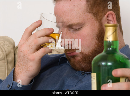 Depressiv müde alkoholischer junger Mann trinkt Alkohol aus einem Glas, Augen geschlossen, Flasche hält Stockfoto