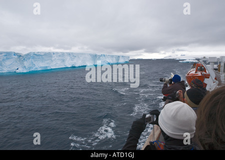 Gesichtslose Touristen fotografieren riesigen Eisberg mit blauen Reflexionen von Schiff im antarktischen Meere Stockfoto