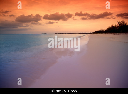 Das türkisblaue Karibische Meer trifft unberührten weißen Sand unter einem dramatischen Himmel bei Sonnenuntergang auf den Bahamas Stockfoto